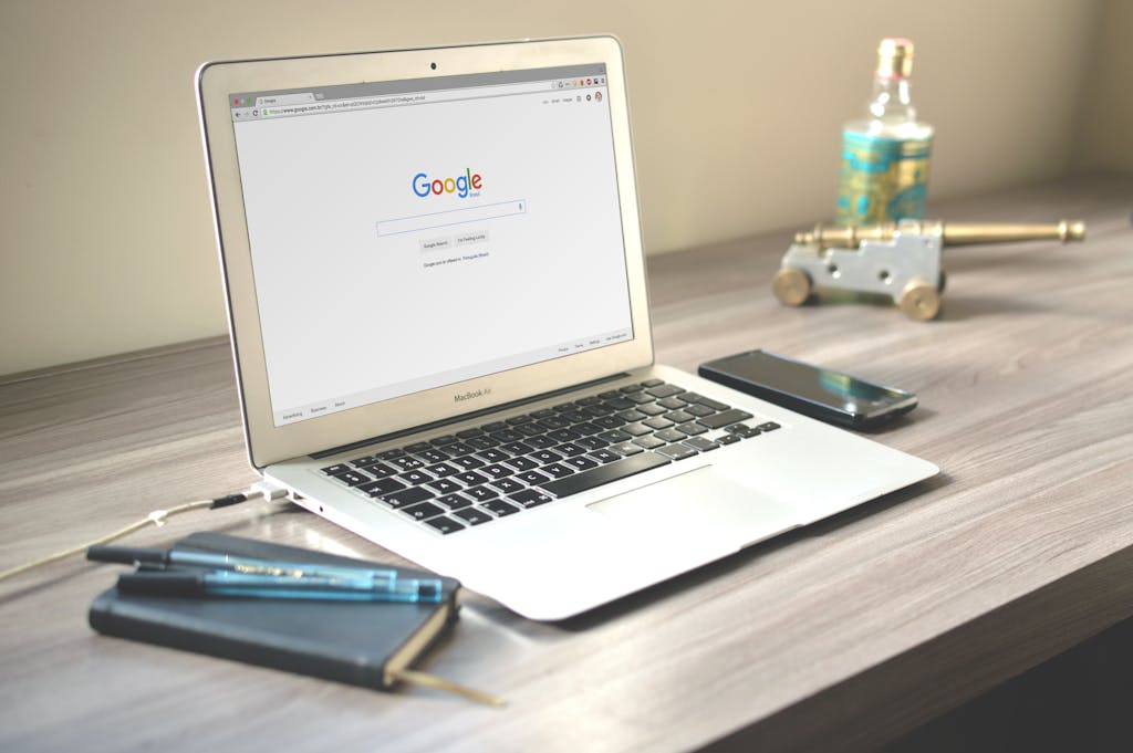 A neat workspace featuring a laptop displaying Google search, a smartphone, and a notebook on a wooden desk. Agencia SEO en Madrid