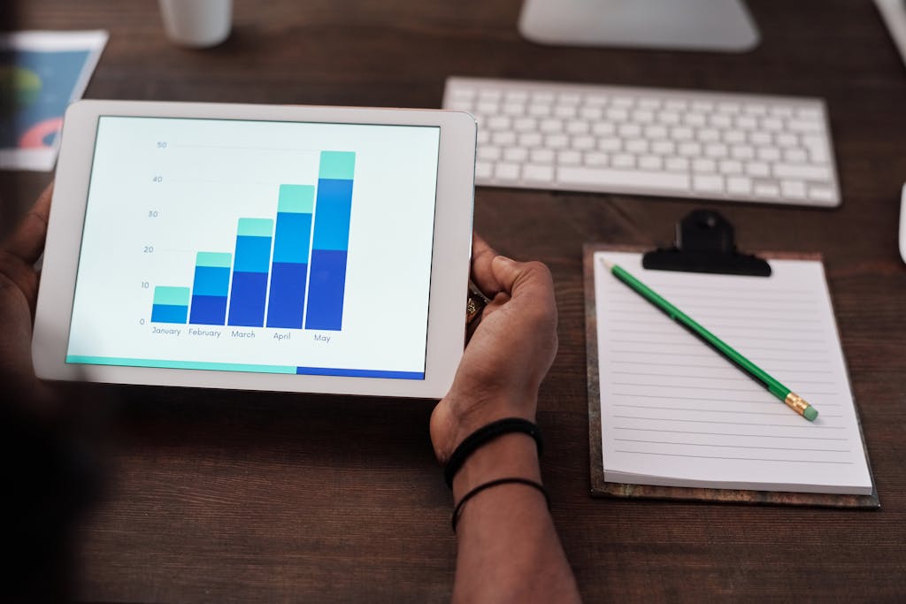 Close-up of a person holding a tablet showing growth charts on a wooden desk setup. Consultoría SEO en Madrid: un servicio estratégico para brillar en Google