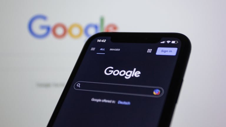 Smartphone screen showing Google search in dark mode with the Google logo in the background.